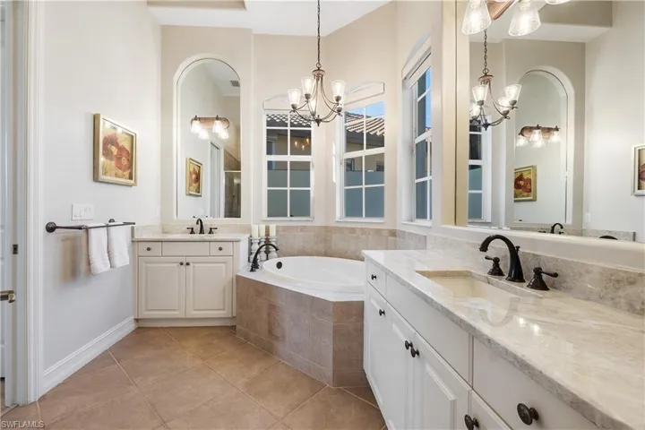 Bathroom featuring tile patterned flooring, vanity, tiled bath, and a notable chandelier