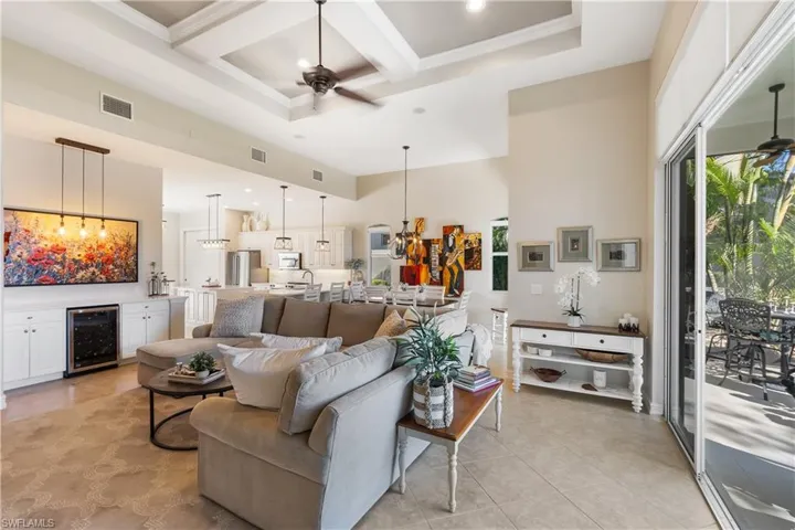 Living room featuring a high ceiling, coffered ceiling, ceiling fan with notable chandelier, and beverage cooler
