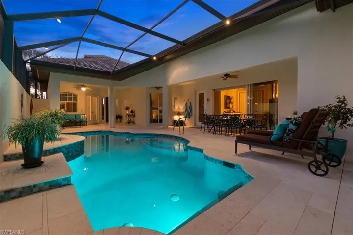 Pool at dusk with ceiling fan, a patio area, and glass enclosure