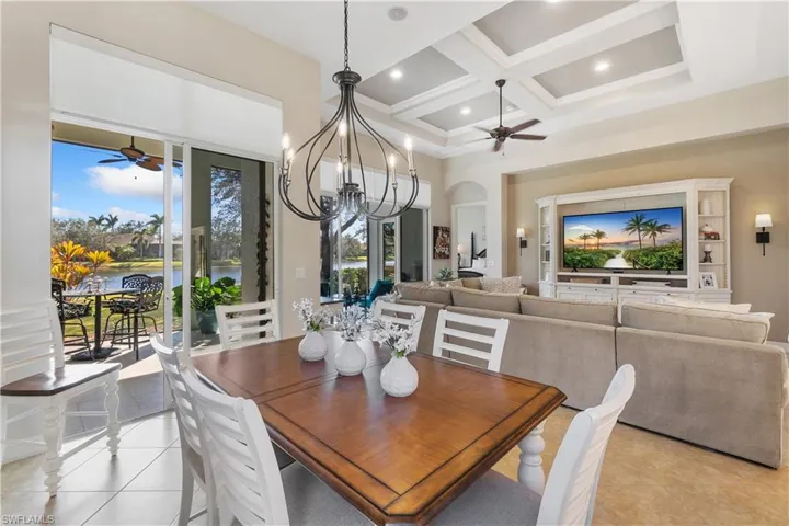 Dining space featuring light tile patterned flooring, a healthy amount of sunlight, coffered ceiling, and ceiling fan with notable chandelier