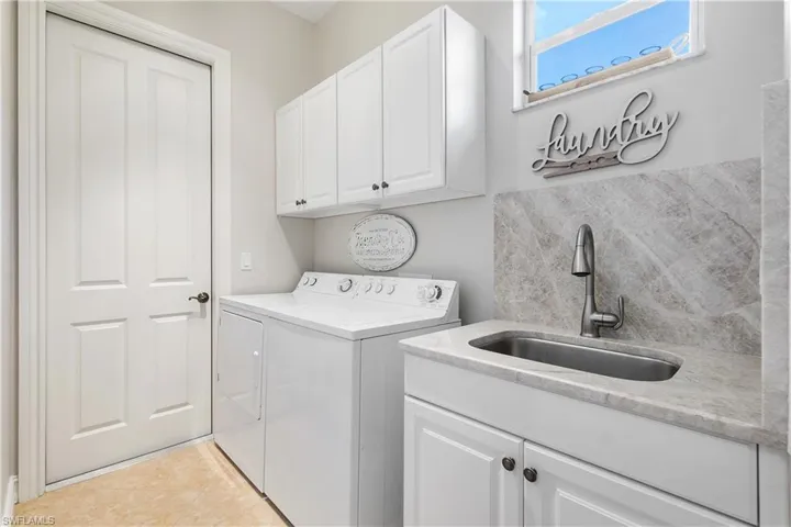 Clothes washing area with washer and dryer, sink, light tile patterned floors, and cabinets