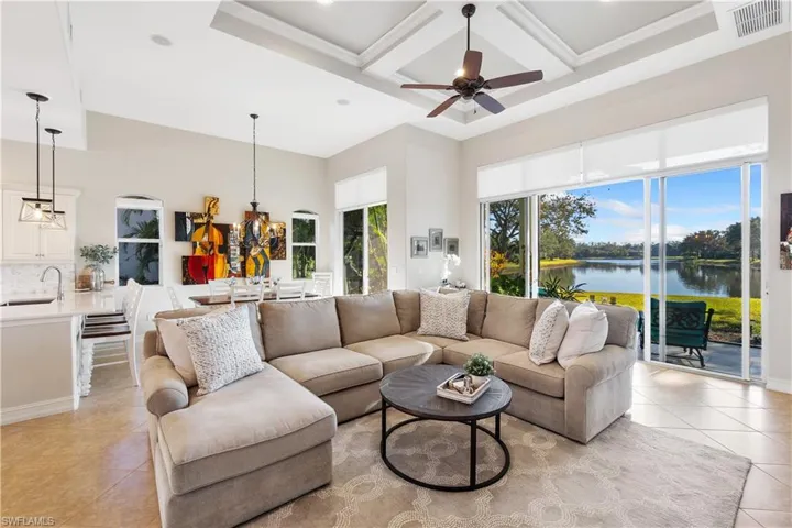 Living room featuring sink, light tile patterned floors, a high ceiling, coffered ceiling, and a water view