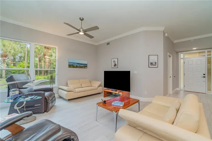 Living room with light tile flooring, ceiling fan, and crown molding