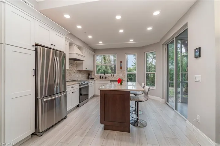 Kitchen featuring custom exhaust hood, white cabinetry, light tile flooring, stainless steel appliances, and a kitchen island