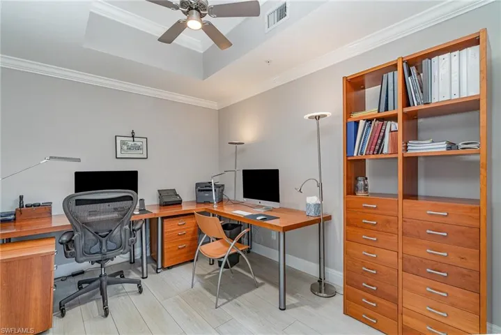 Den with light tile flooring, ceiling fan, a raised ceiling, and crown molding