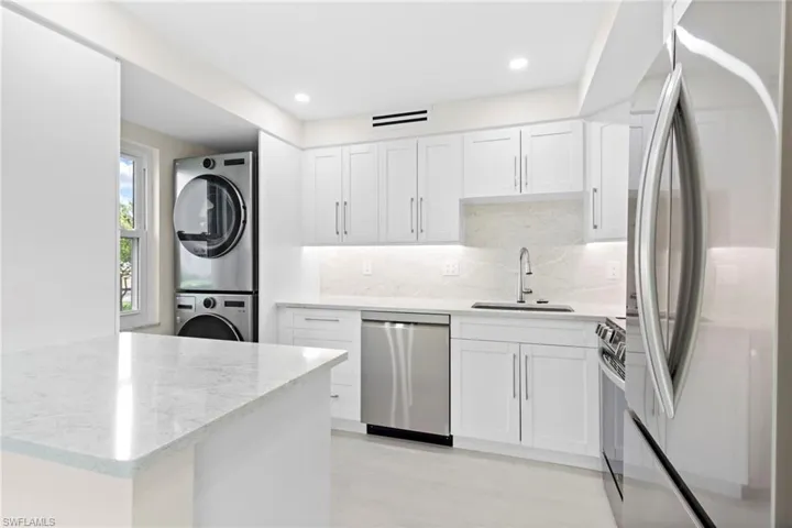 Kitchen featuring sink, appliances with stainless steel finishes, stacked washing maching and dryer, and white cabinetry