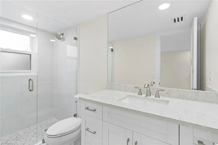 Bathroom with a shower with shower door, vanity, and toilet