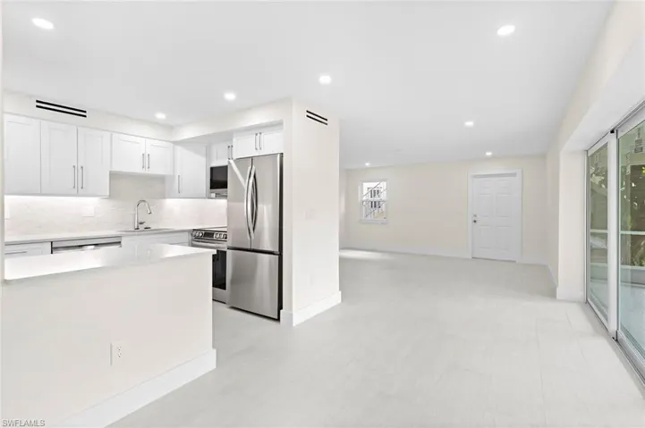 Kitchen with stainless steel appliances, sink, light tile patterned floors, decorative backsplash, and white cabinetry