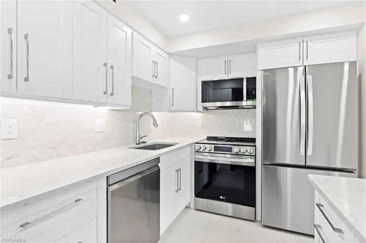 Kitchen with white cabinetry, stainless steel appliances, tasteful backsplash, and sink