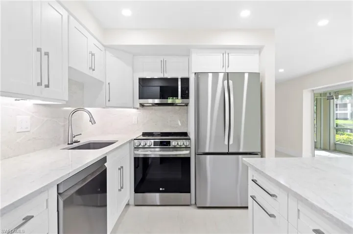 Kitchen featuring tasteful backsplash, white cabinets, light stone counters, appliances with stainless steel finishes, and sink