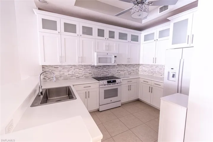 Kitchen featuring white appliances, glass insert cabinets, white cabinets, and backsplash