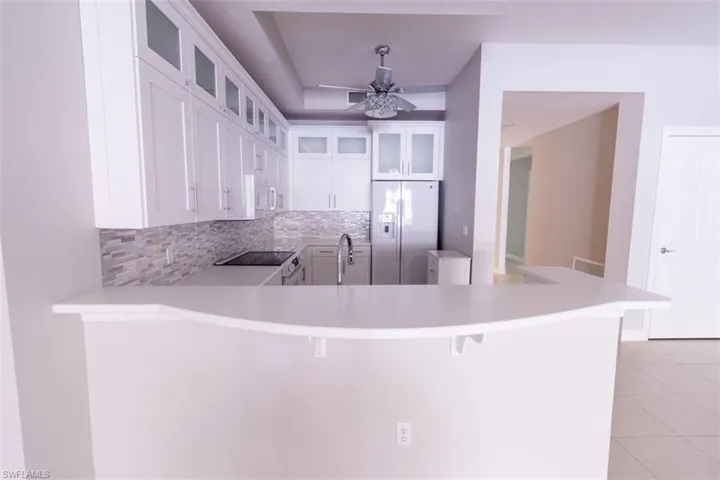 Kitchen featuring decorative backsplash, stainless steel fridge with ice dispenser, white cabinetry, black electric range oven, and glass insert cabinets