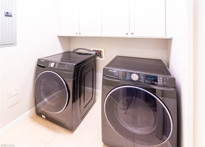 Laundry area featuring electric panel, washer and clothes dryer, cabinet space, and light tile patterned flooring
