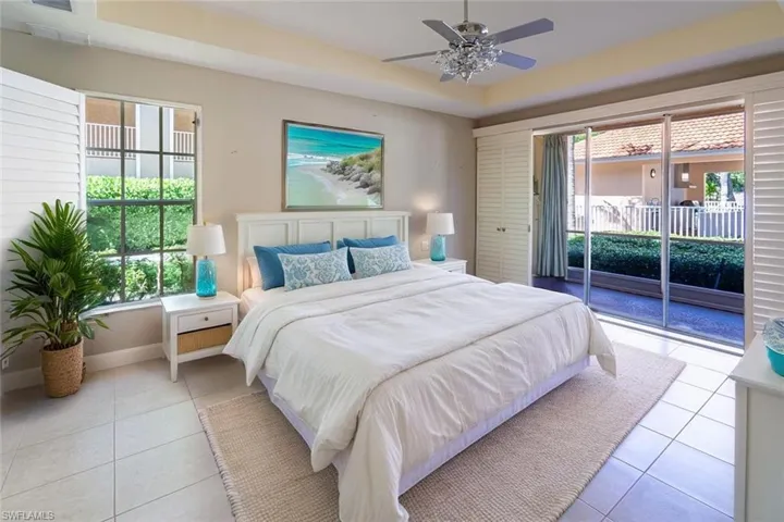 Bedroom with access to outside, a tray ceiling, tile patterned floors, and ceiling fan