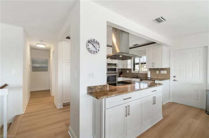 Kitchen with dark stone countertops, light wood finished floors, and white cabinetry