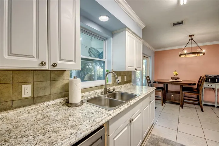 Kitchen with crown molding, white cabinets, decorative light fixtures, light tile patterned floors, and light stone counters