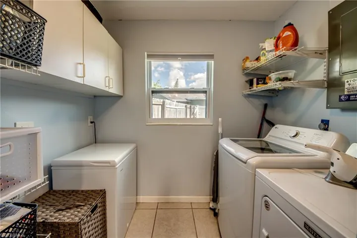 Laundry area featuring light tile patterned floors, electric panel, washer and clothes dryer, and cabinet space