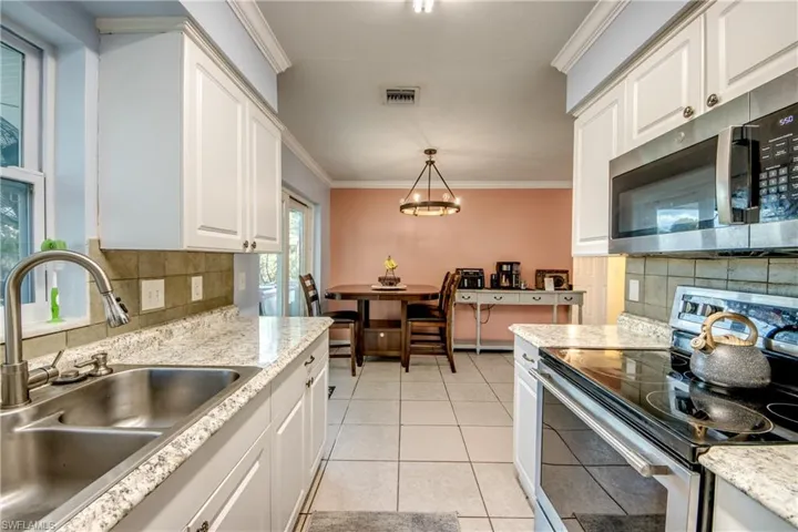Kitchen with appliances with stainless steel finishes, backsplash, ornamental molding, white cabinets, and pendant lighting
