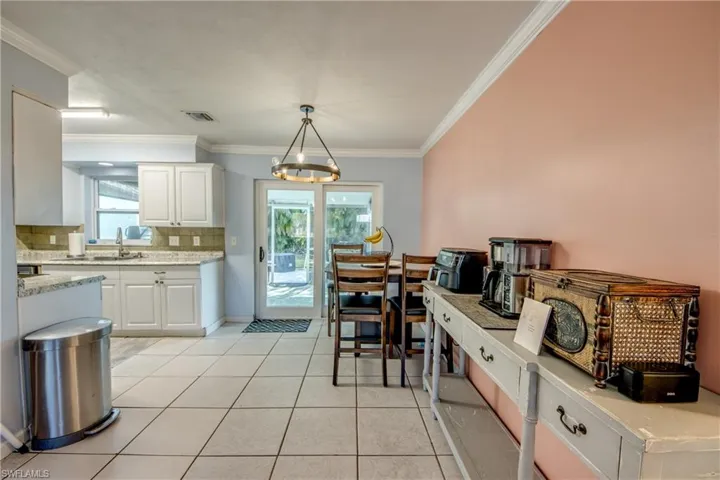 Kitchen featuring white cabinets, light tile patterned floors, plenty of natural light, decorative light fixtures, and crown molding