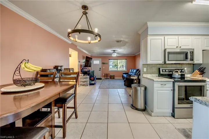 Kitchen with stainless steel appliances, crown molding, white cabinets, light tile patterned floors, and open floor plan