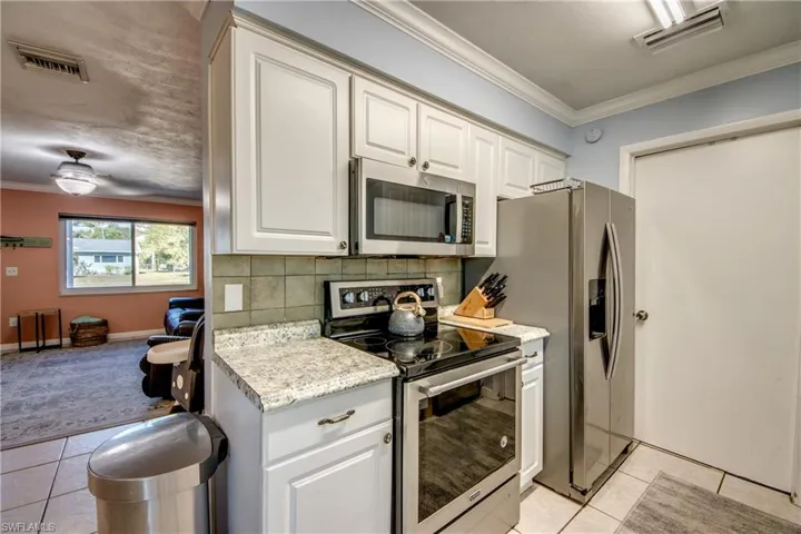 Kitchen with ornamental molding, appliances with stainless steel finishes, light countertops, light tile patterned floors, and backsplash