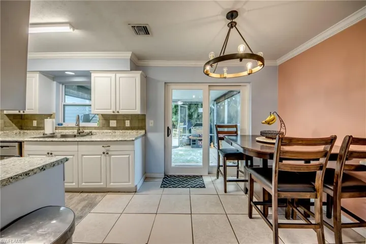 Kitchen featuring white cabinetry, tasteful backsplash, hanging light fixtures, light tile patterned floors, and ornamental molding