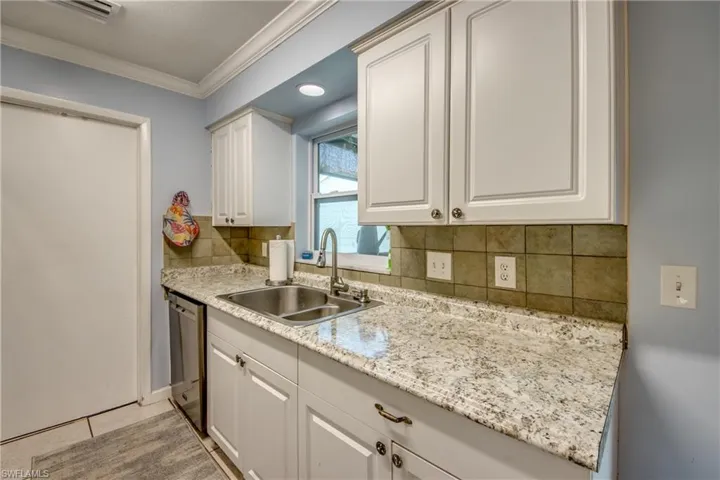 Kitchen featuring ornamental molding, stainless steel dishwasher, white cabinets, tasteful backsplash, and light stone counters