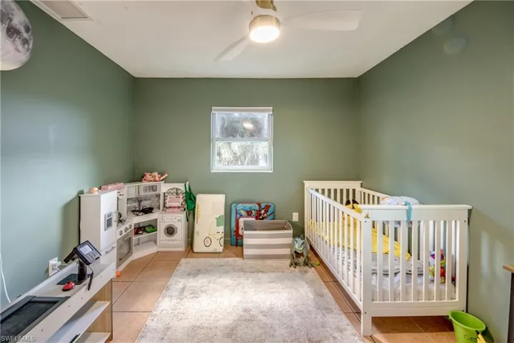 Bedroom with a crib, light tile patterned floors, and a ceiling fan