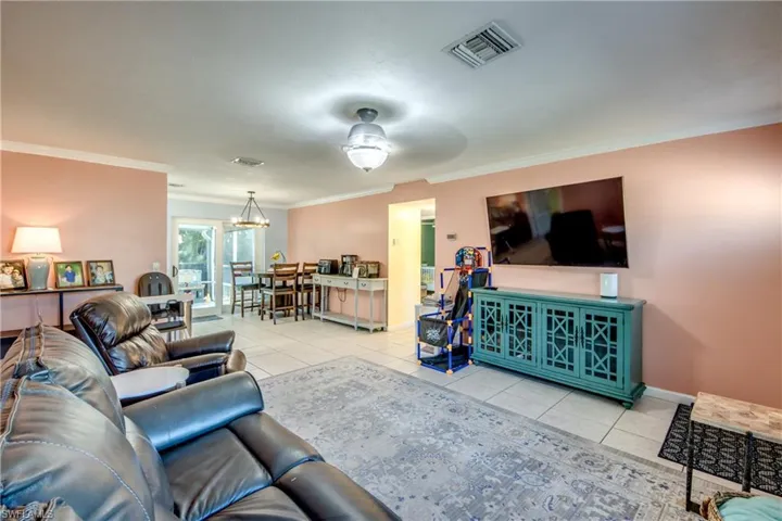 Living room with crown molding, light tile patterned flooring, a ceiling fan, and a chandelier