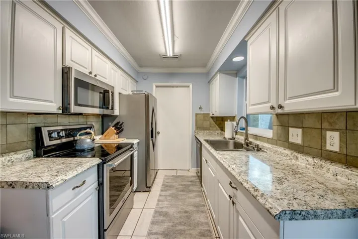 Kitchen featuring appliances with stainless steel finishes, crown molding, white cabinetry, tasteful backsplash, and light countertops