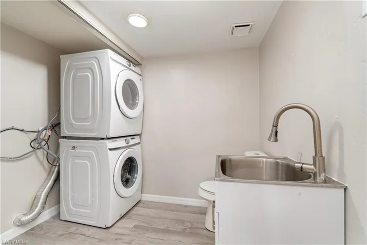 Laundry area with stacked washing machine and dryer and light wood-type flooring