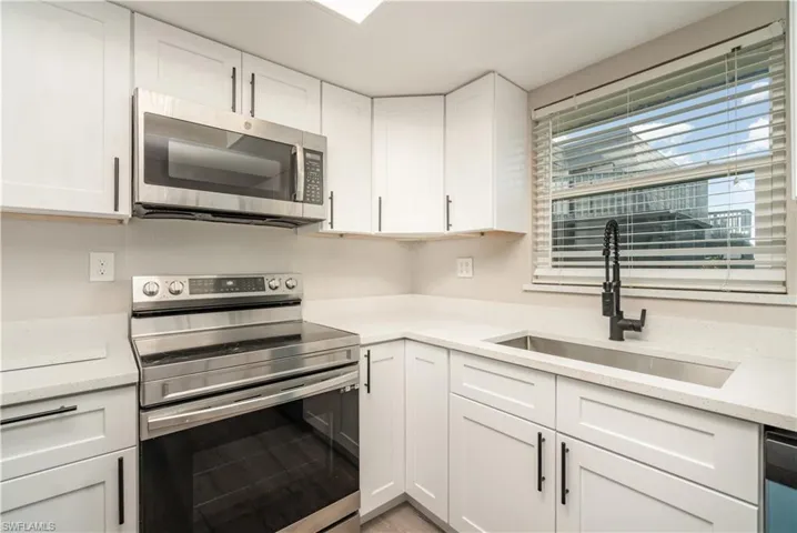 Kitchen with stainless steel appliances, white cabinetry, and light stone countertops