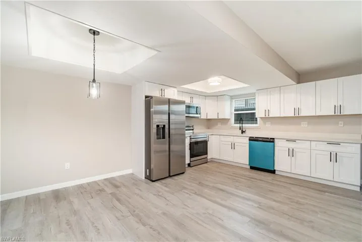 Kitchen featuring stainless steel appliances, white cabinets, hanging light fixtures, and light wood-style floors