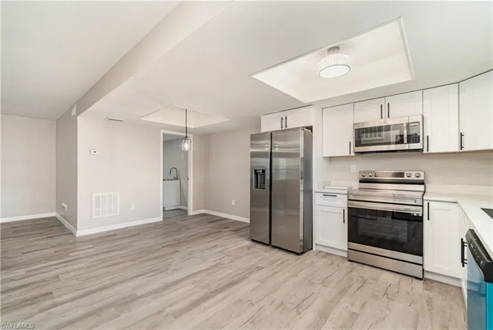 Kitchen with stainless steel appliances, white cabinetry, decorative light fixtures, and light wood-type flooring