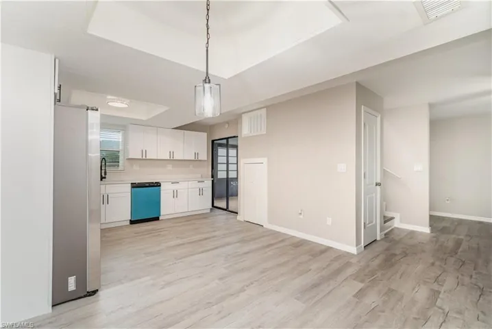 Kitchen featuring light countertops, freestanding refrigerator, white cabinetry, hanging light fixtures, and a raised ceiling