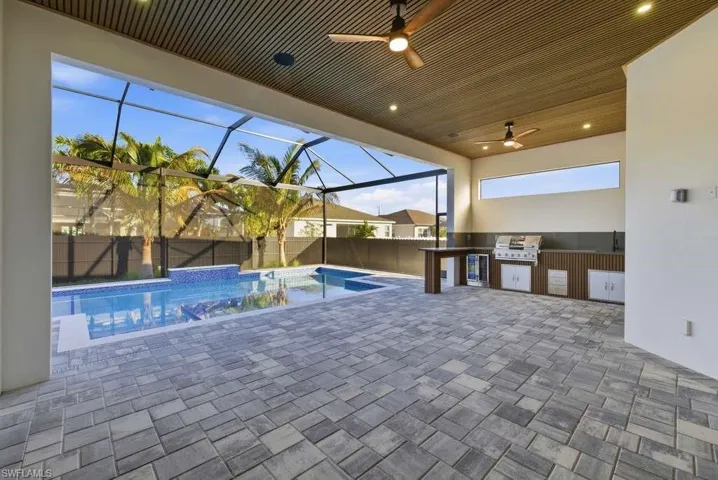 View of swimming pool featuring exterior kitchen, patio surround, a lanai, a sunroom, and a fenced backyard