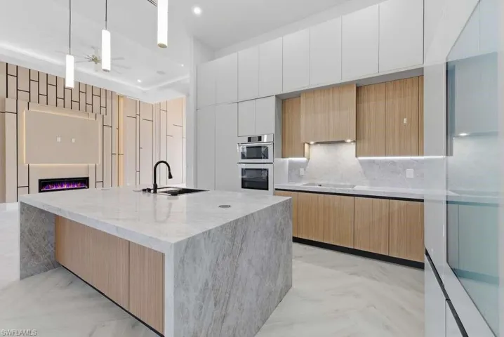Dual tone kitchen featuring modern cabinets, two tone color scheme, a glass covered fireplace, light stone countertops, and hanging light fixtures