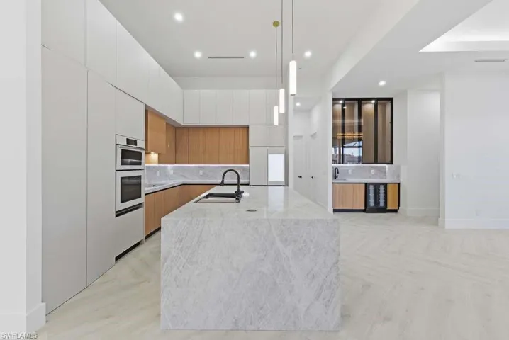 Kitchen featuring dual tone cabinets, modern cabinets, parquet floors, a kitchen island with sink, and decorative light fixtures