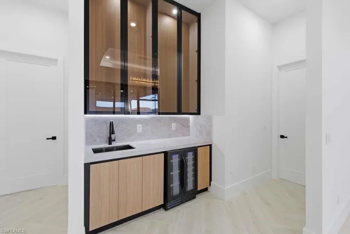 Indoor wet bar featuring light stone countertops, parquet flooring, wine cooler, modern cabinets, and tasteful backsplash