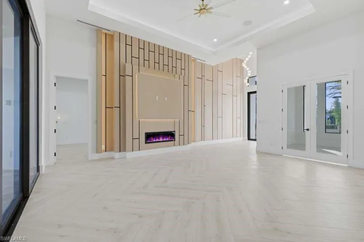 Unfurnished living room featuring french doors, parquet flooring, a glass covered fireplace, a high tray ceiling, and recessed lighting