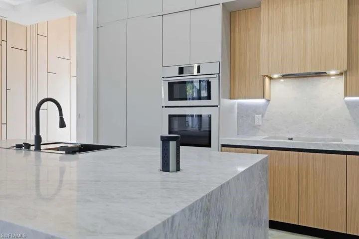 Kitchen with modern cabinets, double oven, light stone counters, extractor fan, and light wood finish cabinetry