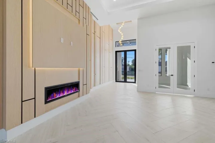 Unfurnished living room featuring french doors, a glass covered fireplace, and a high ceiling