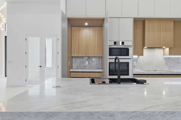 Kitchen featuring modern cabinets, light stone counters, backsplash, double oven, and two tone cabinetry