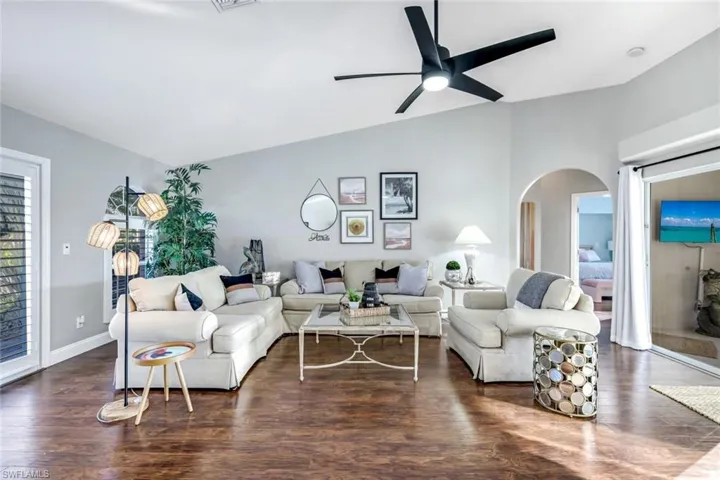 Living area with vaulted ceiling, arched walkways, dark wood-style floors, and ceiling fan