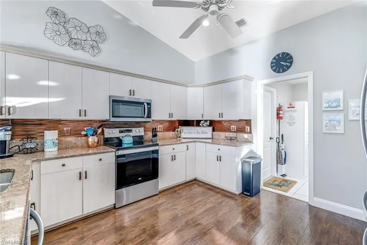 Kitchen featuring stainless steel appliances, tasteful backsplash, dark wood-style flooring, light stone counters, and white cabinets
