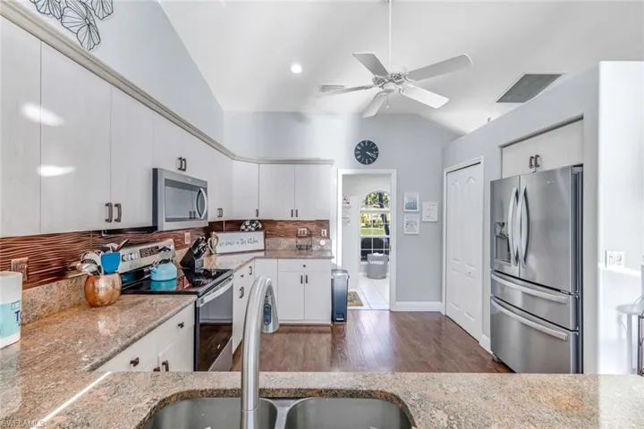 Kitchen featuring stainless steel appliances, decorative backsplash, light stone counters, dark wood-type flooring, and a ceiling fan