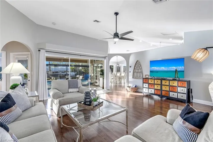 Living area with arched walkways, wood finished floors, ceiling fan, and vaulted ceiling