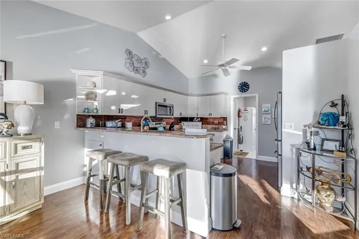 Kitchen featuring dark wood finished floors, a kitchen breakfast bar, backsplash, stainless steel microwave, and high vaulted ceiling