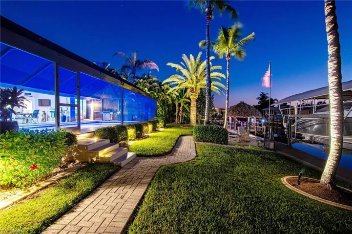 Yard at night featuring boat lift, a lawn, a lanai, and a boat dock