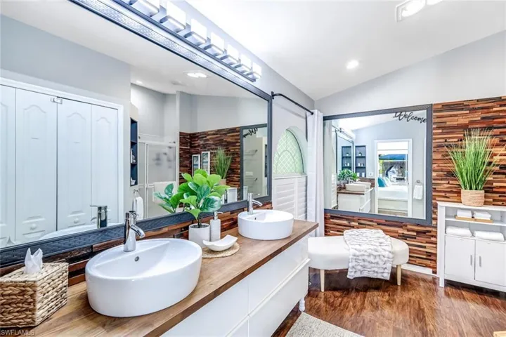 Full bathroom with a stall shower, double vanity, dark wood finished floors, a closet, and lofted ceiling